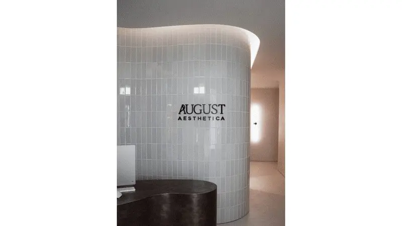 August Aesthetica reception with curved white tile wall and backlit logo